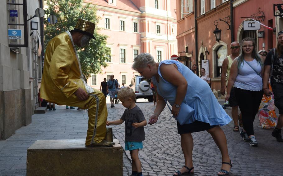 A woman and child show their appreciation for a mime who appears to be sitting on air in Warsaw's old market square in Poland.