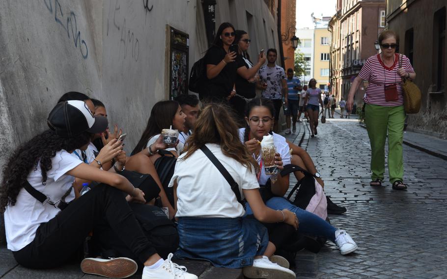 A group of teenagers chat and eat ice cream while sitting on cobblestones in Warsaw, Poland, on Sept. 1, 2019. Soft-serve ice cream is a popular treat in the city.