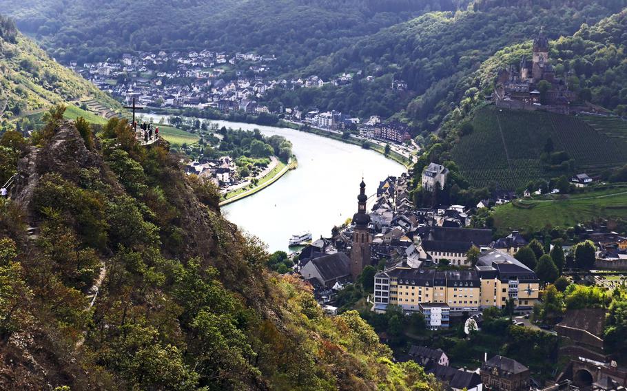 A view of Cochem, Germany, from the chairlift station above the city. At left, people have a look from the viewing platform at the Pinner Cross, the Reichsburg towers over Cochem at right.