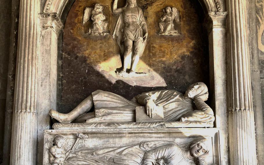 A finely sculpted marble tomb under a covered walkway at the Church of Santa Maria la Nova in Naples, Italy.