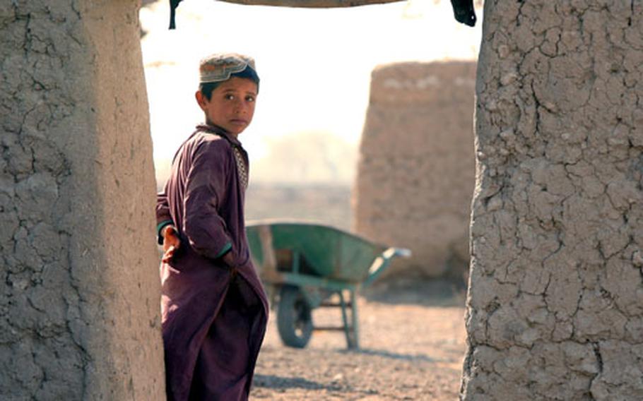 A boy stands in a doorway watching U.S. troops as they talk to an elder in the village of Mama Karez.