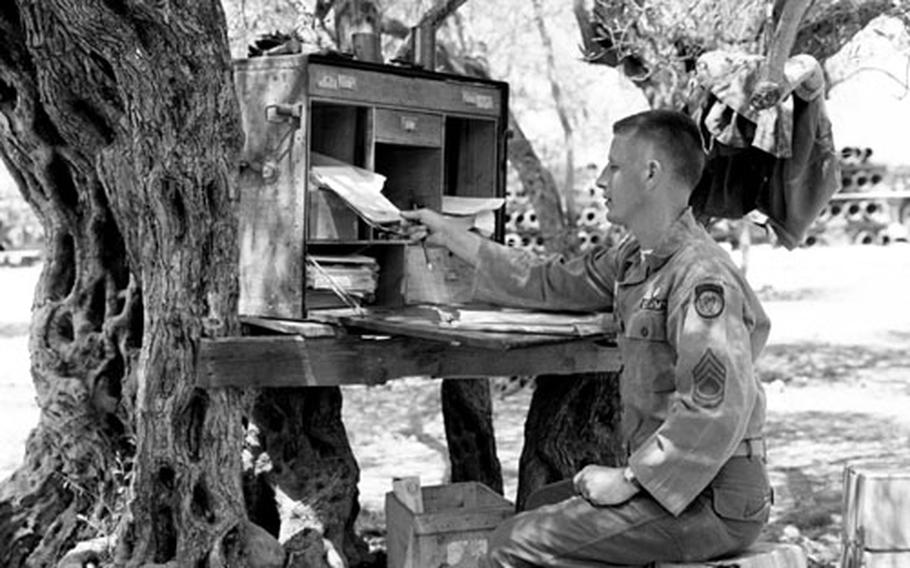 Sfc. Robert Chinn works at his desk beneath an ancient olive tree near Beirut in August, 1958.