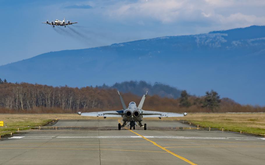 An EA-18G Growler taxis toward the runway at Ault Field as a P3C Orion performs a low approach on March 29, 2019.