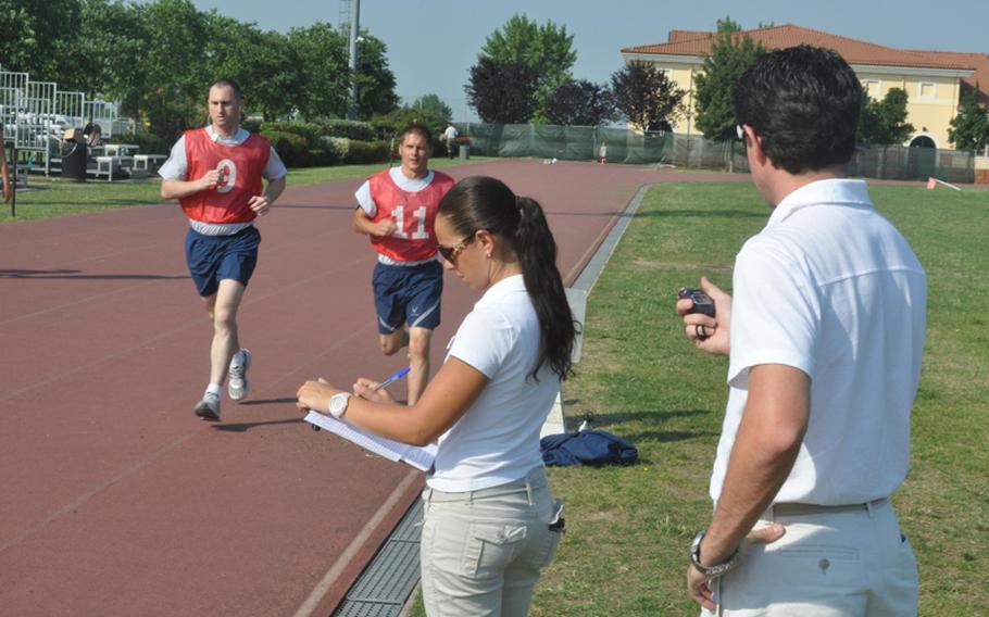 Eleonora Paronuzzi and Luca Rustja keep tabs on Tech. Sgt. Jeremy Tucker, left, and Airman 1st Class Brandon Detter as they run around the track at Aviano Air Base in Italy during the first day of the Air Force's new fitness test.