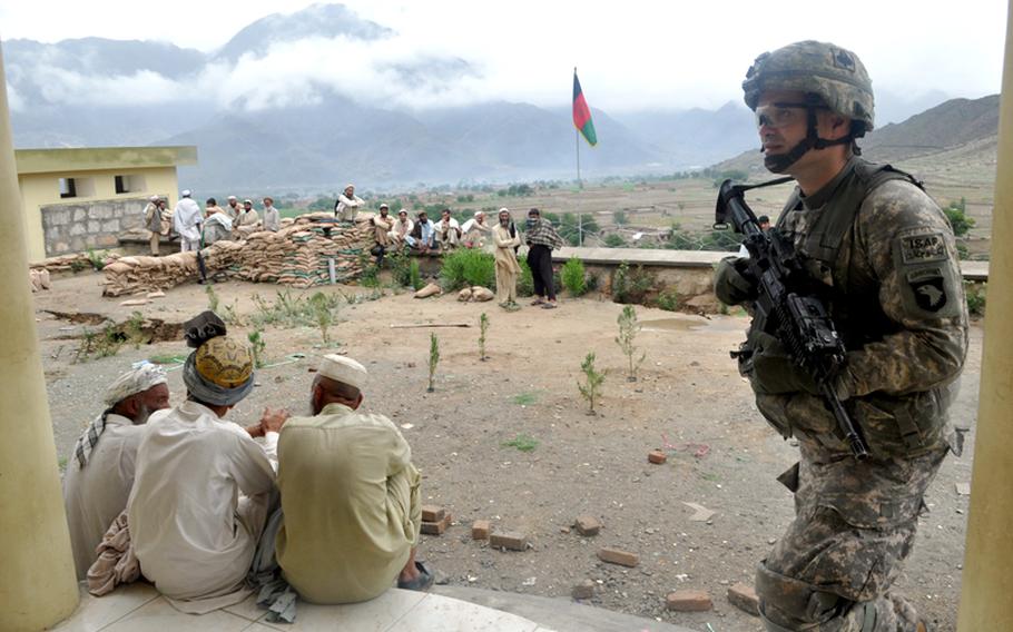A U.S. soldier walks past Afghan villagers outside the Marawara District Center on Aug. 8. The district in Kunar province was the scene of a big U.S.-led offensive to rout insurgents in late June.