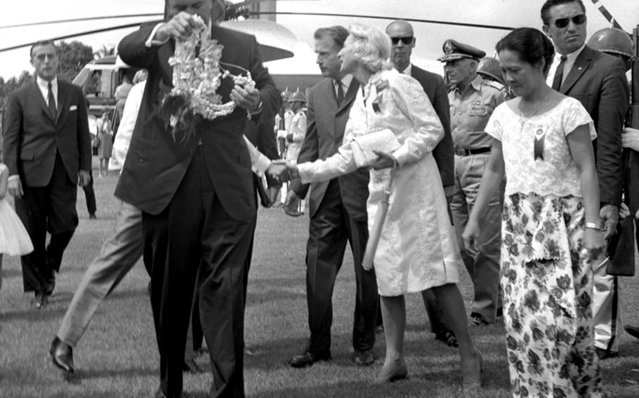 President Lyndon Johnson struggles with a floral arrangement as he arrives at a stop during the Manila Summit.