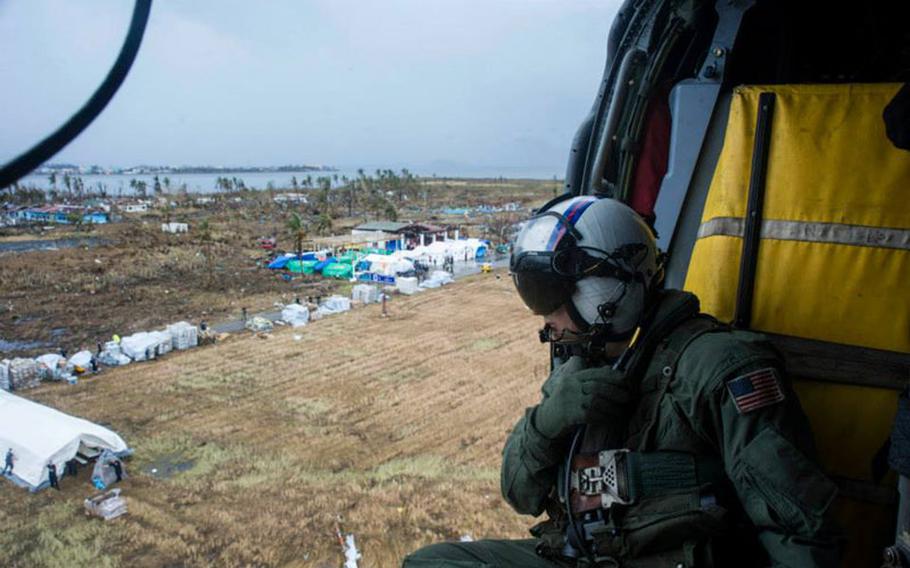 Petty Officer 2nd Class Justin Peach, from Riverside, Calif., prepares to drop supplies from an MH-60S Sea Hawk helicopter from the Golden Falcons of Helicopter Sea Combat Squadron 12, into Tacloban in support of Operation Damayan.