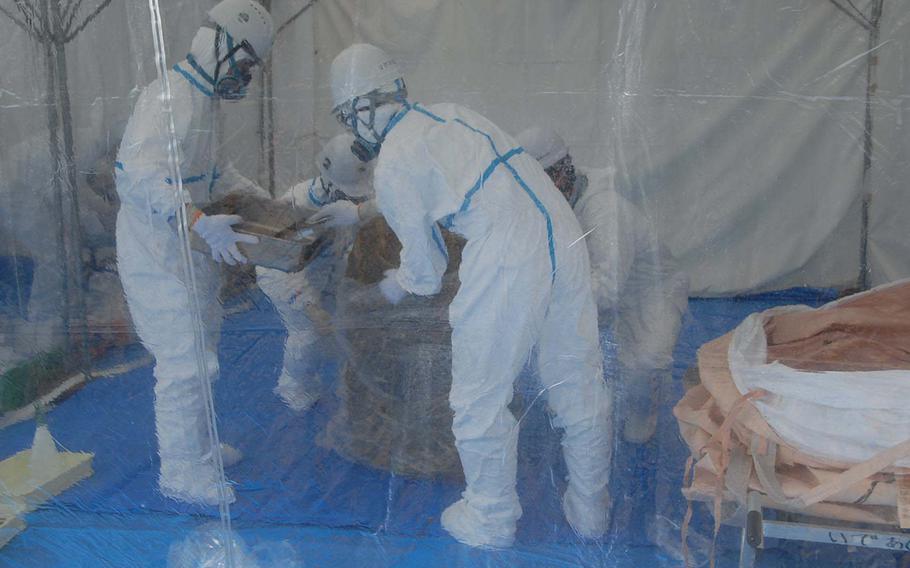 Inside a plastic-draped tent, Japan Ministry of Defense workers examine a badly rusted drum unearthed Jan. 28, 2014, from a soccer field near Kadena Air Base schools where 22 dioxin- and herbicide-laced barrels were found last year.