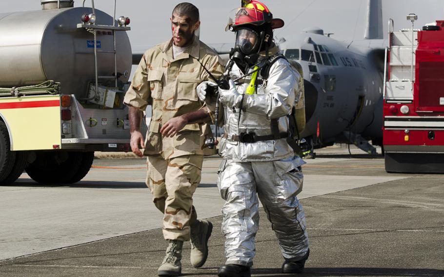 A firefighter from the Yokota Fire Department escorts an aircrewman assigned to the 374th Airlift from the scene of a simulated C-130 Hercules crash at Yokota Air Base March 3, 2014 during the Samurai Readiness Inspection.