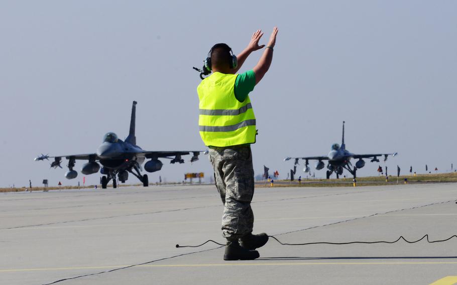 A crew chief guides 555th F-16 Fighting Falcons into place, March 14, 2014, at Lask Air Base, Poland. A total of twelve 555th Fighter Squadron F-16 Fighting Falcons and approximately 200 military personnel arrived in Poland in response to the Ukraine crisis.