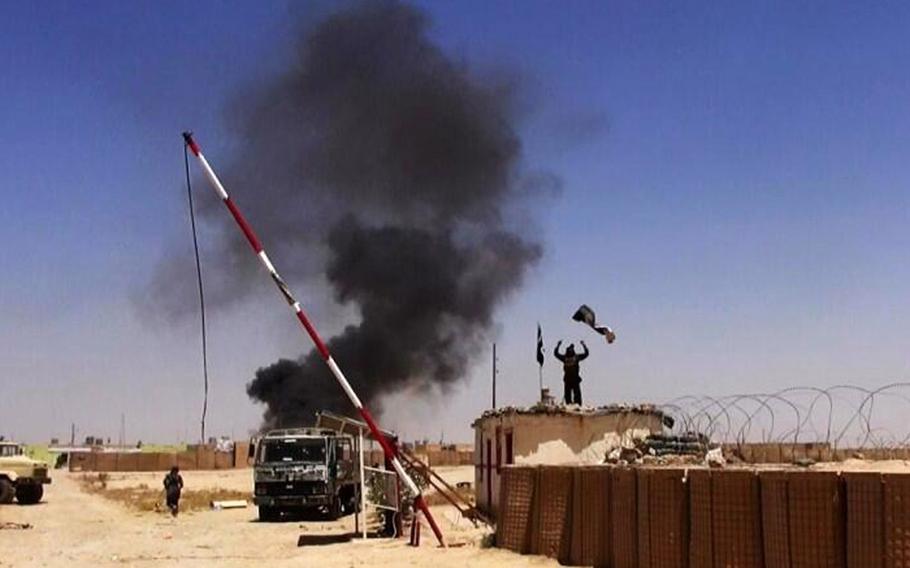 This file image posted on a militant news Twitter account on Thursday, June 12, 2014 shows people from the al-Qaida-inspired Islamic State of Iraq and the Levant (ISIL) raising their flag at the entrance of an army base in Ninevah Province, Iraq.