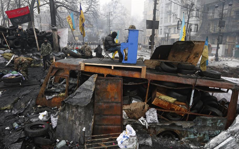 Vladyslav Musiienko, "Ukraine, Maydan" | Ukrainian protester plays piano on a barricade in front of the riot police line during the continuing protest in Kiev, Ukraine, on Oct. 2, 2014.
