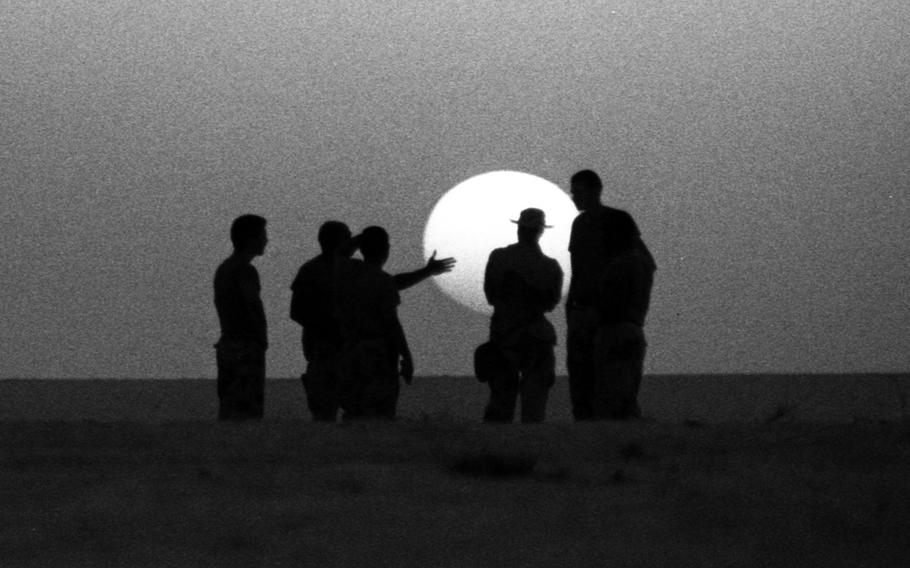 American servicemembers deployed to the Saudi desert during Operation Desert Shield in January, 1991 are silhouetted against the setting sun as they discuss the issues of the day.