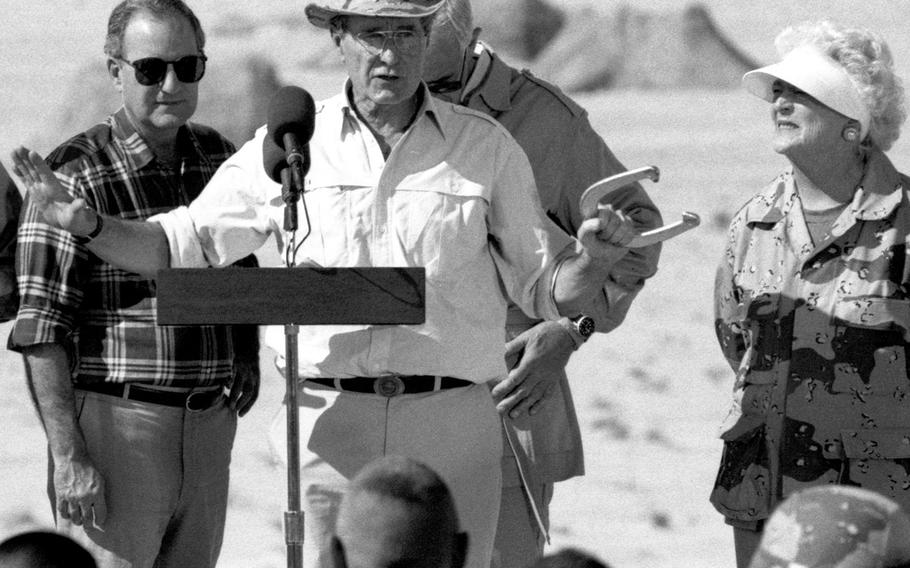 President George H.W. Bush holds a key element of one of his favorite sports as he talks to U.S. troops at a base in the Saudi Arabian desert during Operation Desert Shield in November, 1990. At right is first lady Barbara Bush.