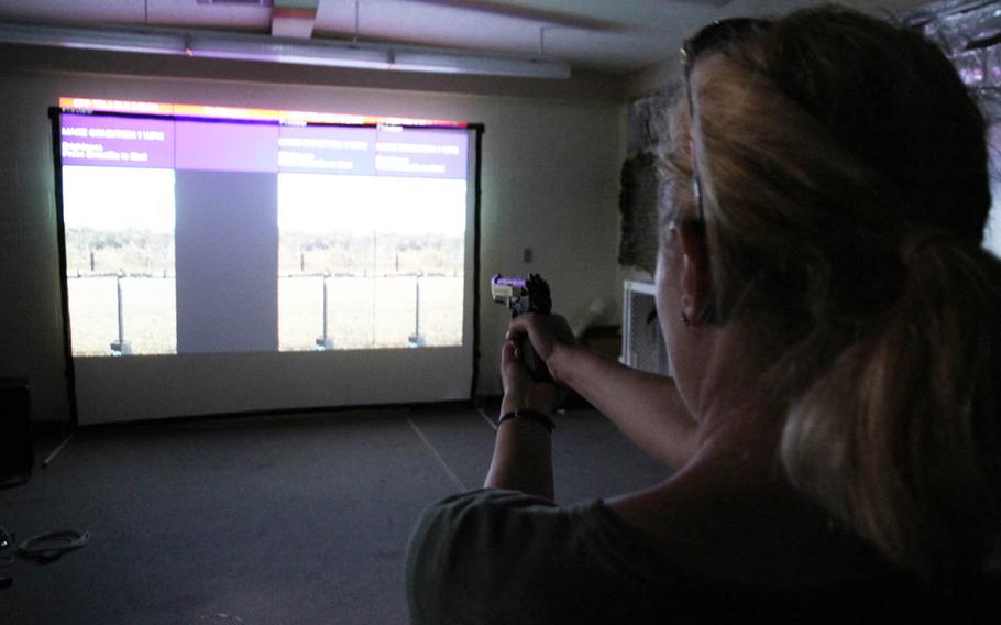 Marine Corps spouse Jena Haycock take aim in an Indoor Simulated Marksmanship Training simulator at Marine Corps Air Station Futenma in Okinawa, Japan, Friday, May 13, 2016, during the second-annual Marine Air Control Group 18 Spouses Warrior Day. Clips in the pistol use compressed air to simulate live rounds.