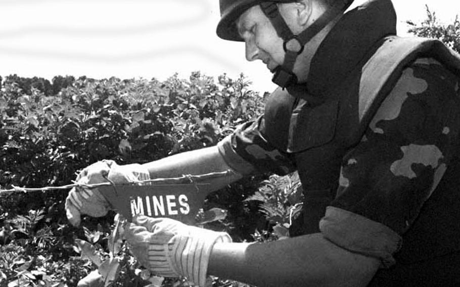 Pvt. Ilija Mamic, a Bosnian soldier, hangs a metal mine awareness sign on an area designated as a mine field off Route Arizona in Bosnia and Herzegovina following the arrival of NATO peacekeepers in 1996.