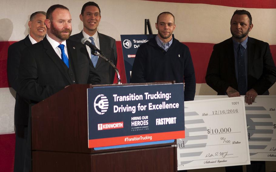 Navy veteran Troy Davidson addresses a crowd inside the U.S. Chamber of Commerce Foundation after being announced the winner of a $150,000 Kenworth semi-truck Friday, Dec. 16, 2016. Kevin Scott, an Army veteran, and Russell Hardy, a veteran of the Army and Navy, stand behind Davidson holding $10,000 checks they were awarded as runners-up in the competition, put on by Hiring our Heroes, Kenworth and FASTPORT.