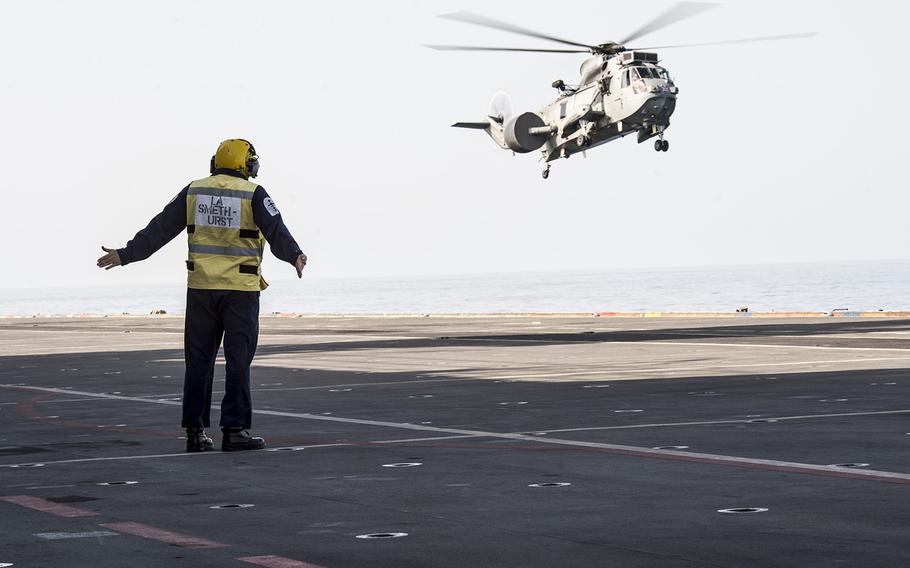 A flight deck crew member aboard the Royal Navy helicopter carrier HMS Ocean directs a Sea King MK7 airborne surveillance and control helicopter landing on the ship during exercise Unified Trident in the Persian Gulf Jan. 31, 2016. 
                Chris Church/Stars and Stripes