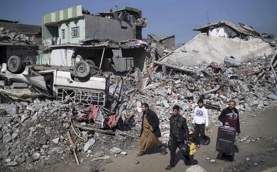 Iraqis walk past debris of houses destroyed during fighting between Iraqi security forces and Islamic State militants on the western side of Mosul, Iraq, Friday, March 24, 2017.