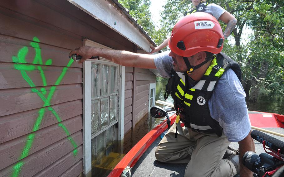Perched on a boat, Team Rubicon volunteer Anthony DiToma marks a house in a flooded neighborhood of Beaumont, Texas as checked after pounding the roof to make sure no one was trapped inside on Sept. 2, 2017. The water was still up to rooftops but had started to recede.