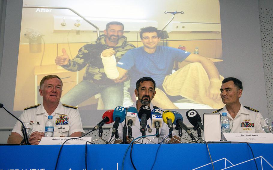 A photo of Dr. Pedro Cavadas posing with a sailor whose hand was amputated is projected on a screen. In hte foreground, Adm. James G. Foggo III, commander of U.S. Naval Forces Europe-Africa and commander of Allied Joint Force Command Naples, Italy, left; Cavadas, a neurosurgeon at Hospital de Manises in Valencia, Spain, center; and Capt. Michael McGinnis, U.S. Naval Forces Europe-Africa Force Surgeon, answer questions at the hospital May 4, 2018.