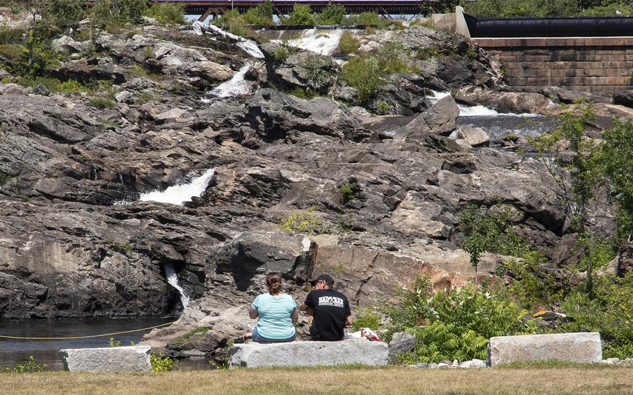 Two visitors to Veterans Memorial Park in Lewiston, Maine, in August, 2019 sit on benches overlooking the Androscoggin River's Great Falls.