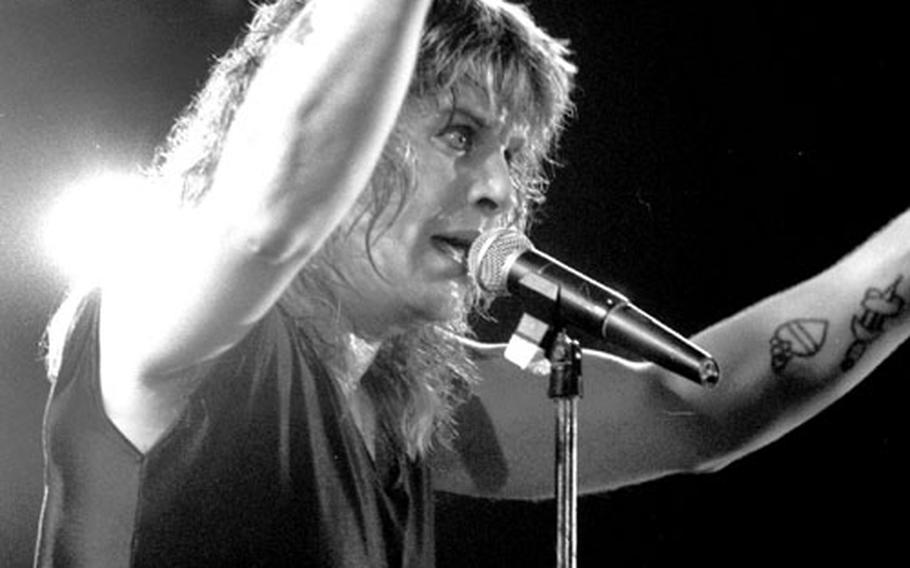 Ozzy Osbourne raises both arms during a concert.