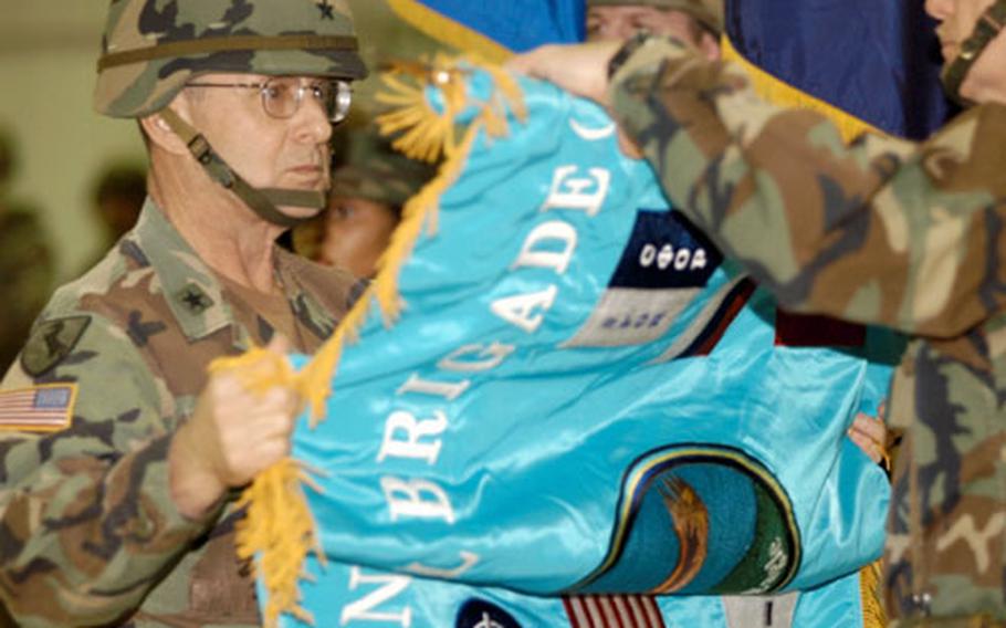 Brig. Gen. John von Trott unrolls the new Multinational Brigade North flag. Multinational Division North officially changed the name to "brigade" on Friday.