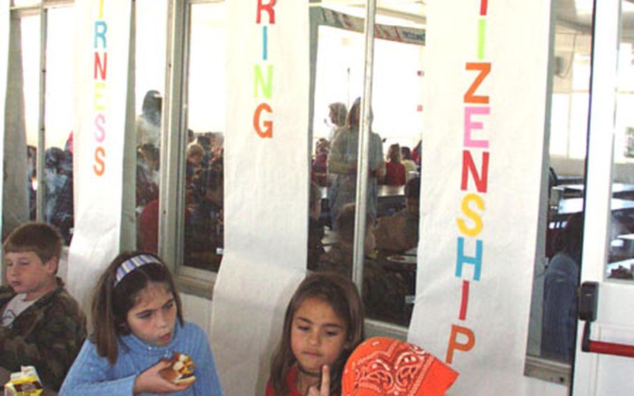 Third-graders Alisha Schiermeyer, Alyssa Toney, and Tamela Queen eat lunch Monday at Naval Station Rota, Spain, in front banners signifying three of the six pillars of character. The base's elementary school along with all Defense Department schools in the Mediterranean School District have adopted "Character Counts!" The character-building program is popular among schools in the United States.