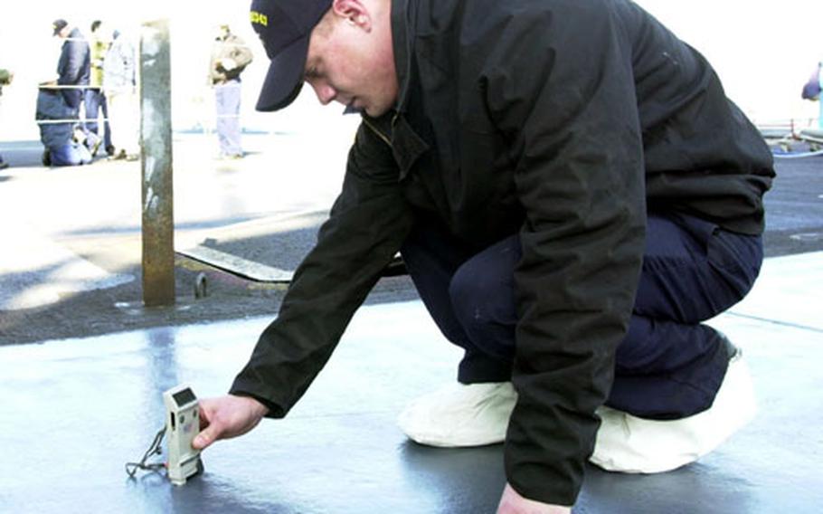 Airman Stephen Lutz, a quality assessor on the USS Kitty Hawk, checks the thickness of paint applied to the flight deck Monday after the crew had applied layers of paint and a new, non-skid surface.