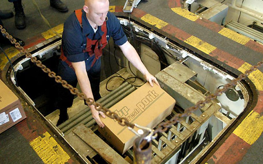 Airman Gary McIntosh lowers food supplies onto a conveyor belt in the hangar bay during an underway replenishment on the USS Kitty Hawk.