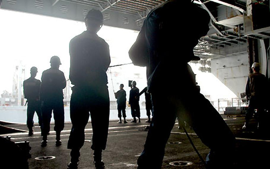 Crew members aboard the Kitty Hawk keep a grip on a 200-foot phone line connecting it to the replenishing ship. The line handlers pull on the half-inch thick line if the ships drift together, and slack it if the ships move apart.