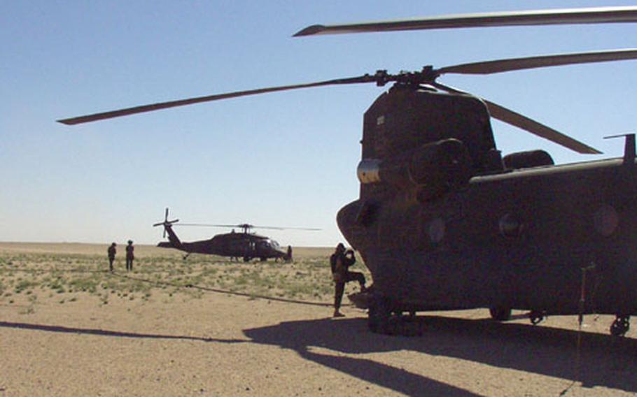 Crew members from a Black Hawk helicopter, left, hook up to a Chinook during a fat-cow refueling exercise in the Kuwaiti desert.