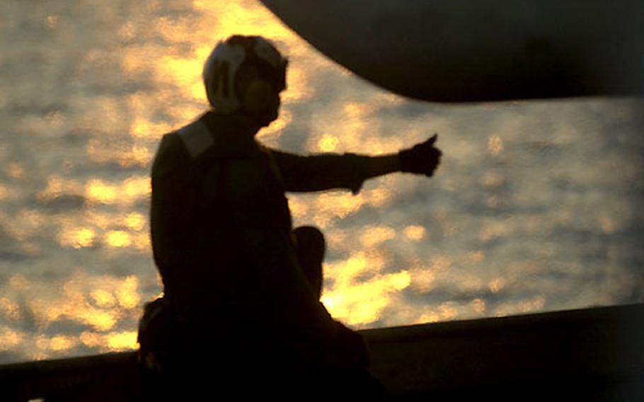 An aircrew member gives a thumbs-up during flight operations at sunset Monday on the Kitty Hawk.