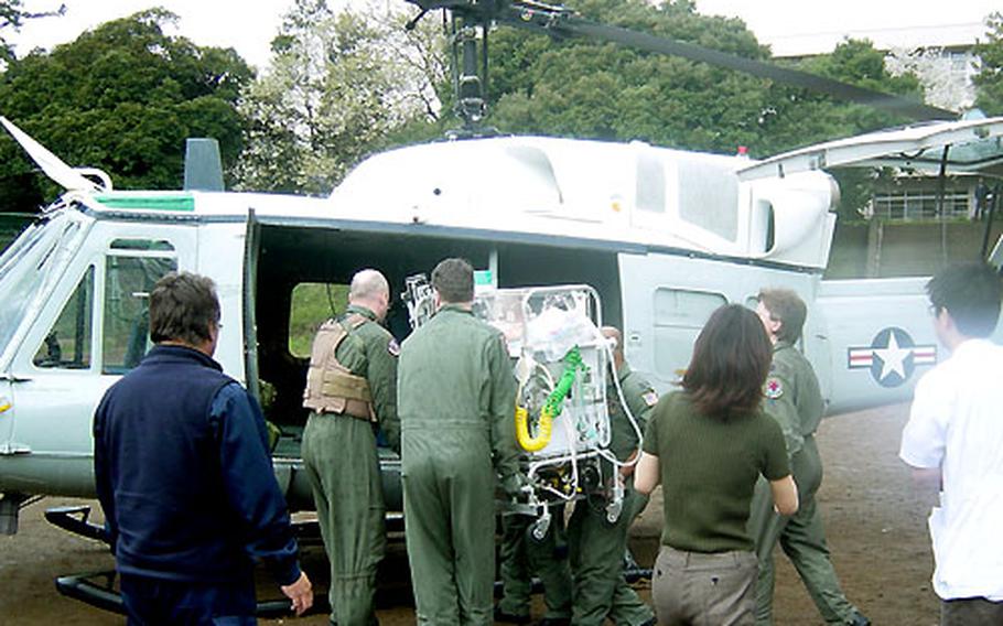 Members of Yokota Air Base’s 459th Airlift Squadron, who landed a UH-1N Huey on this baseball field in Yokohama, Japan, load an incubator holding an infant in need of medical care in the States.