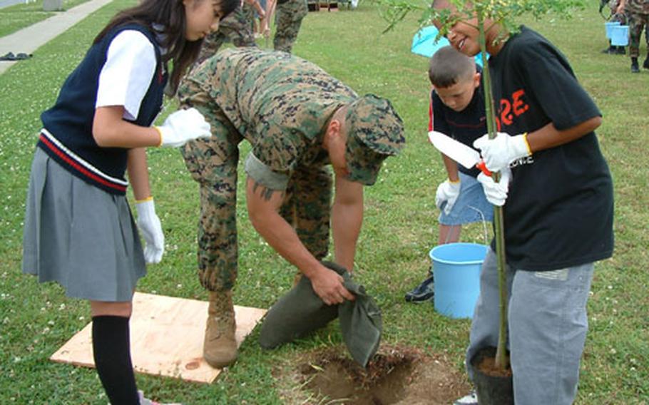 Marine Lance Cpl. Shaun Barefoot helps elementary school pupils Reina Ikema, Kyle Johnson and Malcolm Donato plant a tree Tuesday during an Earth Day event on Camp Foster, Okinawa. Okinawan youngsters from Chatan joined Killin Elementary School pupils in the planting of 80 trees along Stillwell Drive.