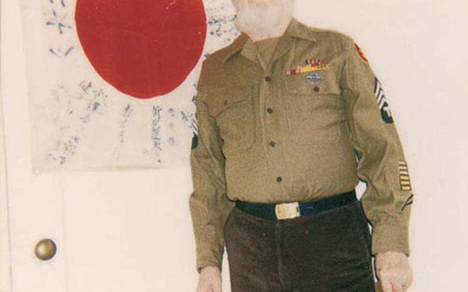 Former Army combat medic Robert H. Walsh poses in front of the Japanese battle flag which was recently returned to its hometown.