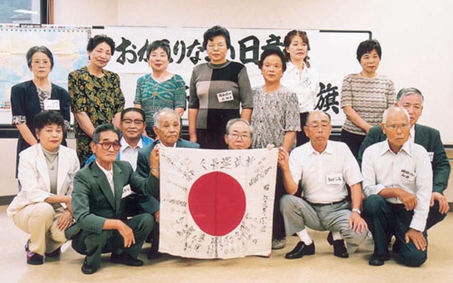 People who signed the Japanese battle flag along with family members and the town mayor gather around the flag after it was returned to them last week.