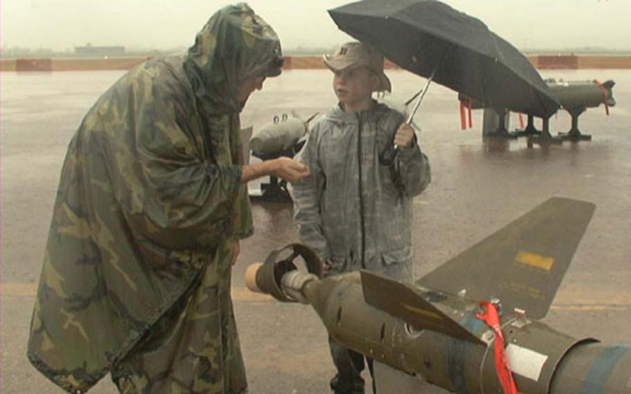 On the rainswept flight line at Osan Air Base, South Korea, Maj. Chuck West covers a few fine points about bombs with his son Andrew, 9, a fourth-grader at Osan American Elementary School. West is with the 303rd Intelligence Squadron. Although rain forced cancelling the base's second annual Air and Space Power Day, father and son braved a drenching for a look at the aircraft and ordnance that had been set up for display.