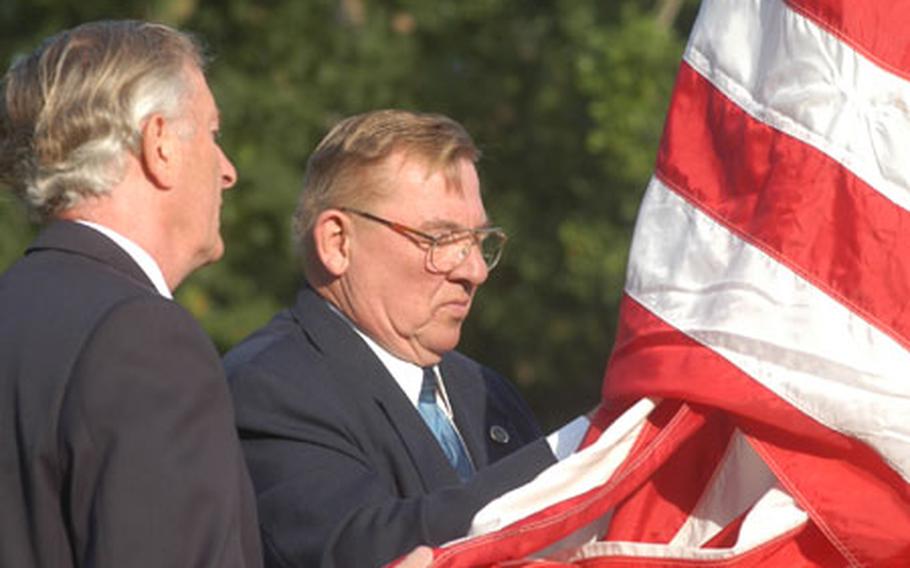 Bob Stone, left of the Royal British Legion, and Jim Schoenecker, superintendent of the Cambridge American Cemetery, raise a flag early Thursday at the cemetery. The flag belongs to an American veteran's widow and once flew above the White House. The ceremony also marked events of Sept. 11, 2001.