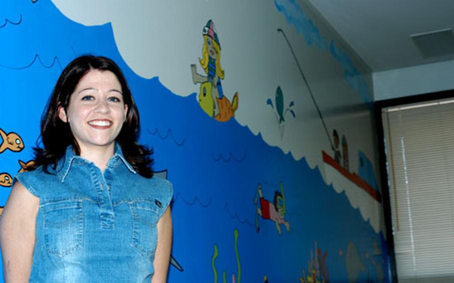 Melodie E. Lopez, designer of the new mural painted by the Sigonella Mom’s Club, stands with the finished project in Naval Hospital Sigonella’s pediatric ward. The NAS Sigonella Religious Ministries Department funded the mural.