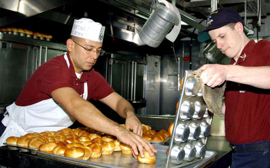 Petty Officer 1st Class Luis R. Martinez, left, and Petty Officer 3rd Class Mike Mears arrange cloverleaf rolls Wednesday in preparation for Thanksgiving dinner on the USS La Salle in Gaeta, Italy.
