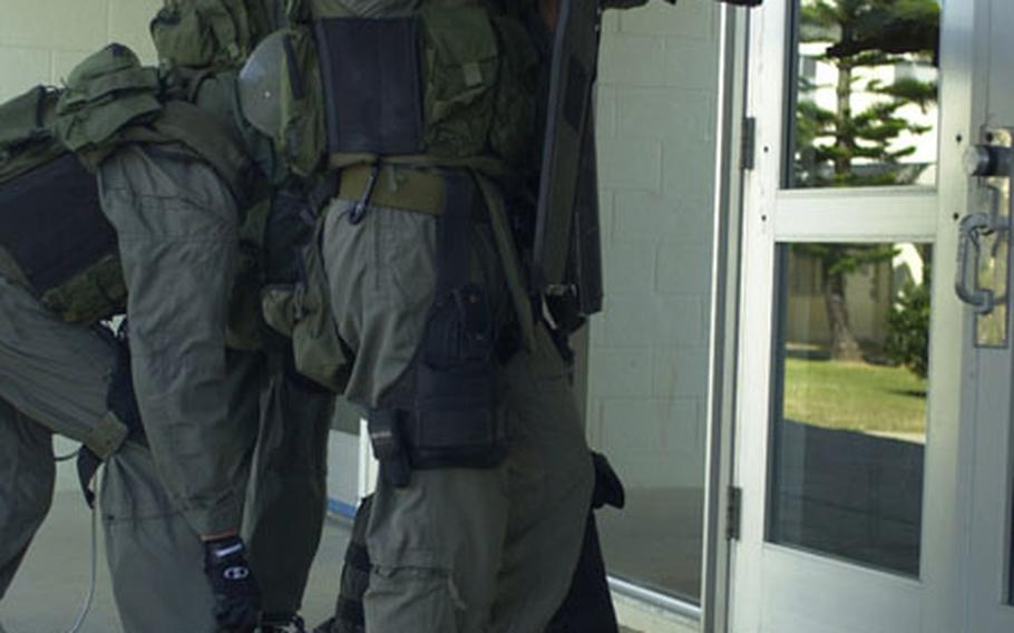 The Special Reaction Team stands guard in front of the Kubasaki High School gymnasium as a team member drops a phone for the hostage taker during Tuesday's practice exercise.