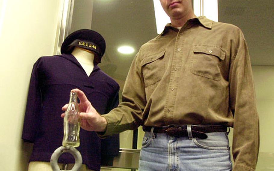 Phil Eakins, Sasebo Naval Base Museum curator and base historian, found the Coca Cola bottle he's holding, along with several others, hidden under floorboards in an old warehouse a few years ago. The bottle has no scratches or chips. Last year, while reading a World War II verteran's book, Eakins said, he realized why the bottles probably were hidden in the crawl spaces: Servicemembers may have been sneaking soft drinks and concealing the empties.
