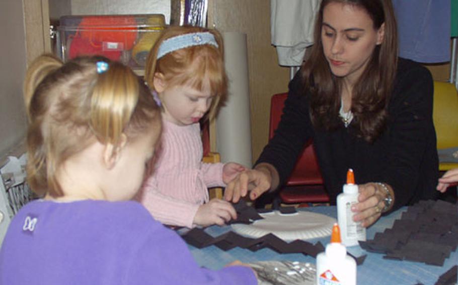 Angela Hamilton, a teacher with the Time for Tots program on Rhein-Main Air Base, Germany, helps children make paper spiders out of construction paper and paper plates.