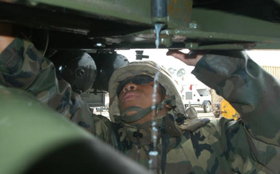 Straining to reach, and soaked to the skin, Spc. Grady Dailey, 20, of Hampton, Va., digs out hidden dirt under his truck at Camp Doha, Kuwait.