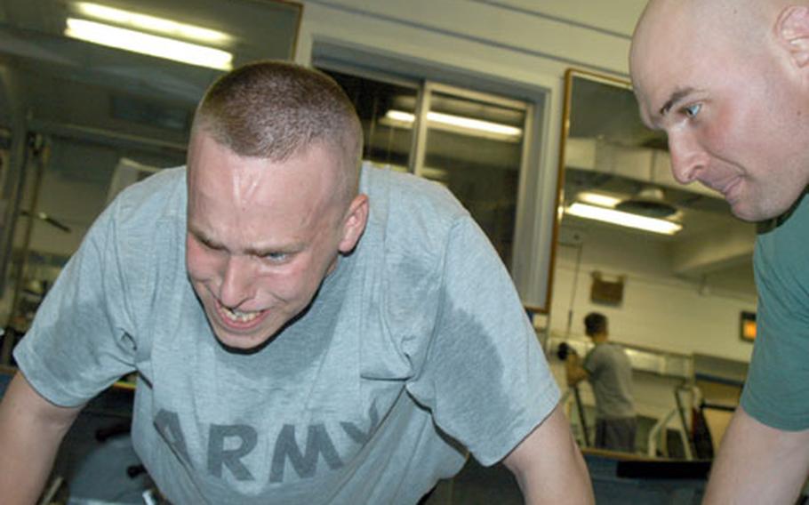 Pfc. Chris Robb shows the strain as he does push-ups under the watchful eye of Staff Sgt. Bryan Baker at the Camp Red Cloud gym.