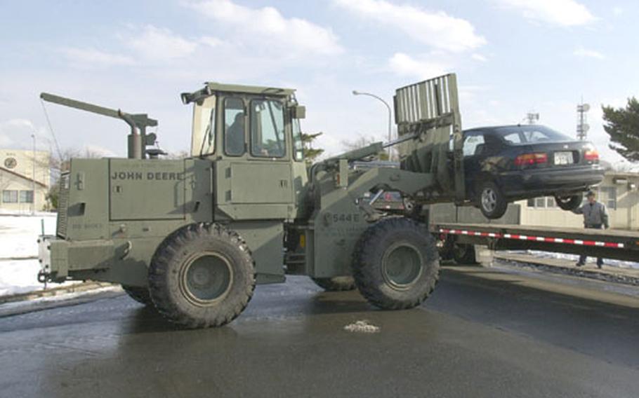 A car is fork-lifted onto a flat-bed truck to make room for snow plows to remove snow from a nearby dormitory parking lot.