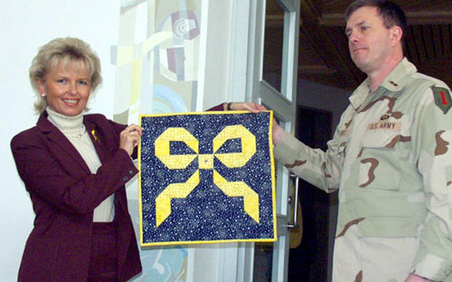 Col. Paul Wentz, commander of the 1st Infantry Division’s Division Support Company, presents a yellow ribbon quilt to Tamara Bischof, the Landratsamt (commissioner) of Kitzingen county in Germany. Bischof said the quilt will hang in the foyer of Kitzingen’s county administration building until all 2,100 Kitzingen-based U.S. Army troops return home safely from Iraq in the spring of 2005.