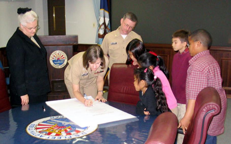 Sasebo Naval Base's Chief Staff Officer Cmdr. Carol Shivers takes her turn signing a Sasebo Elementary School proclamation Wednesday in the base headquarters to designate March as Read Across America Month. Also attending the signing ceremony were, left to right, Principal Stacy Blevins, Command Master Chief Petty Officer William Lowman, and pupils Sherlyn Nocon, 9, Melissa Malong, 8, Wylene Cox, 6, Andrew Racek, 11, and Torey Dugas, 11.
